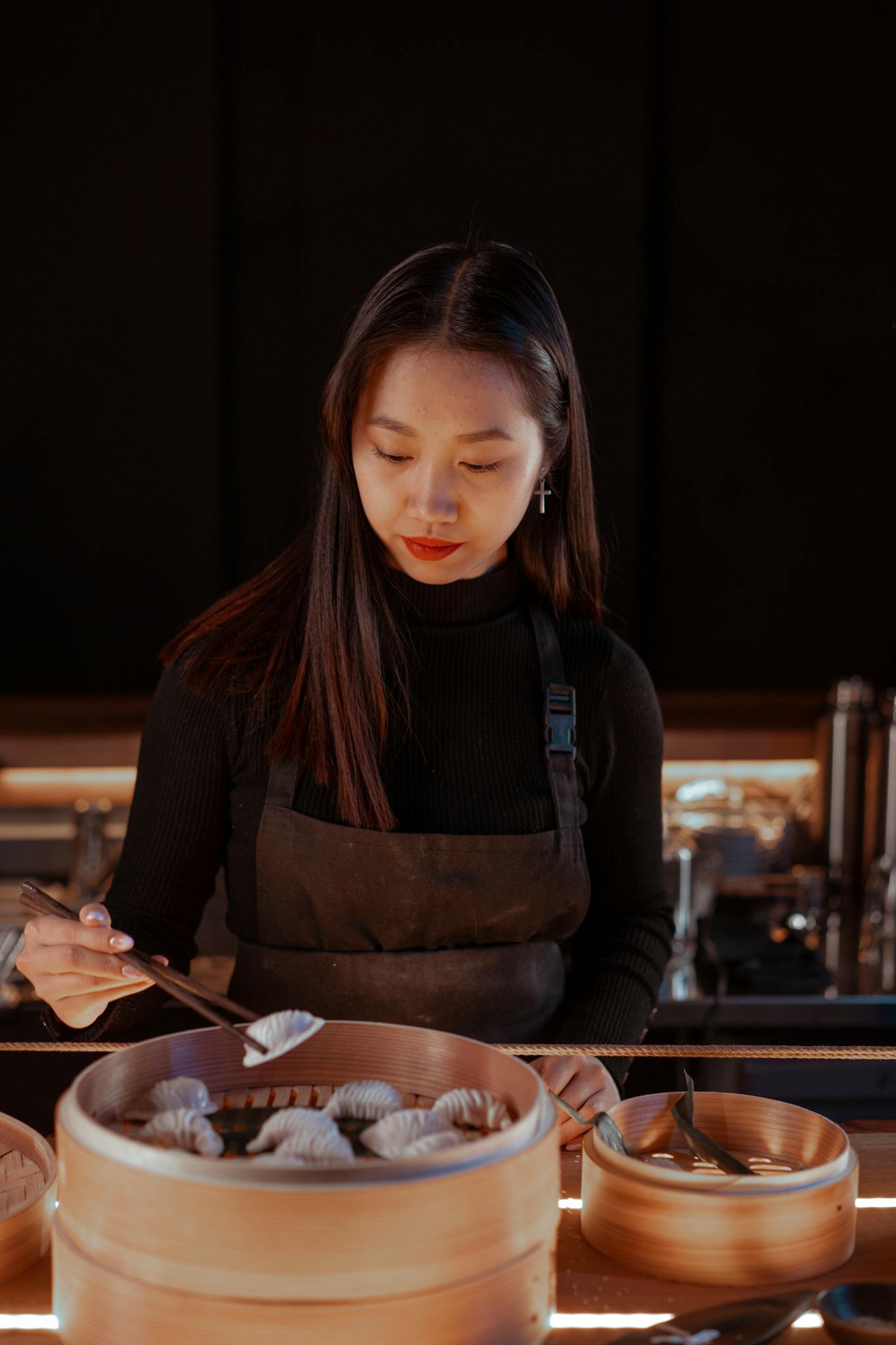 An Asian woman in a restaurant kitchen carefully preparing dumplings, showcasing culinary skills.